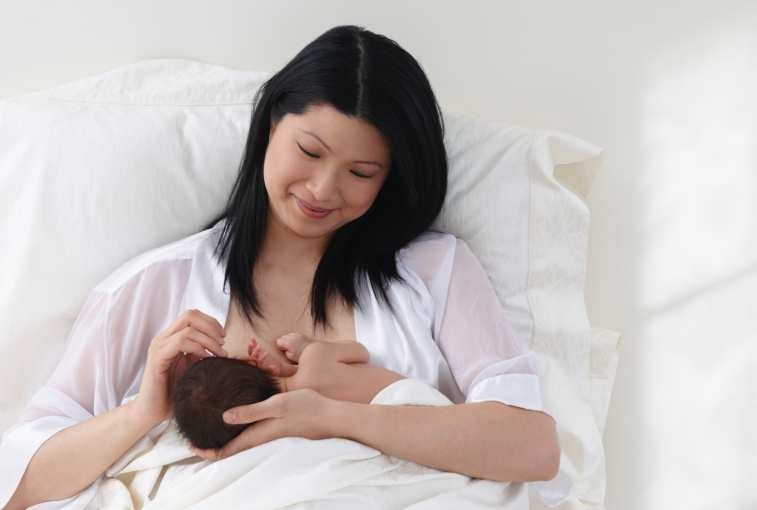 Chinese mother breastfeeding baby in bed