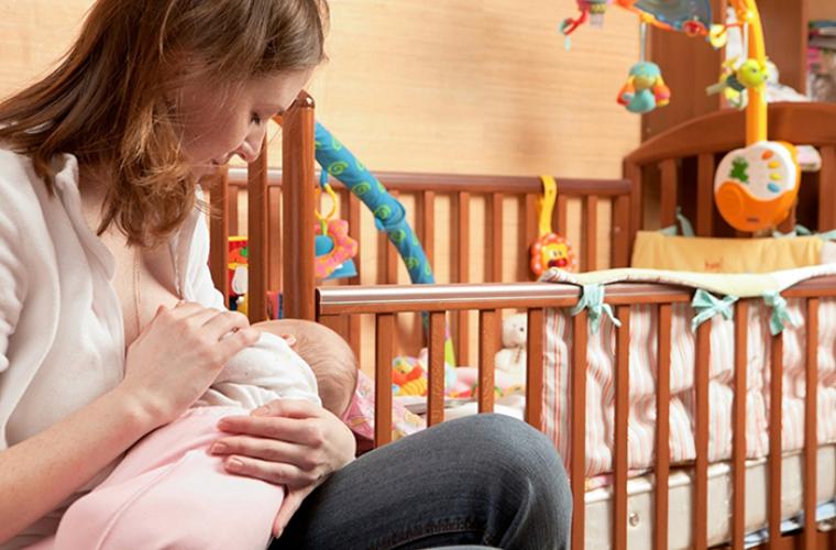 mom breastfeeding next to a crib
