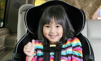 little girl giving a thumbs up in a car seat