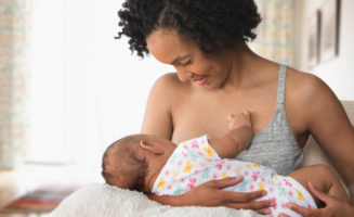 Mom sits in bed while breastfeeding new baby