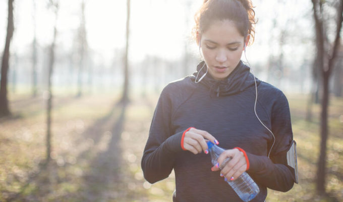 Female athlete at winter,opening bottled water, wearing smart phone around arm, lens flare.