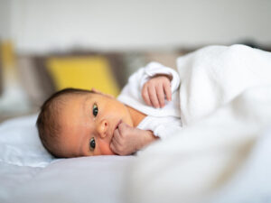 Newborn baby lying on bed, looking around and sucking fingers.