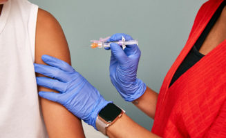 Fu shots are important in pregnancy. A closeup of a woman's arm about to get a vaccine from a doctor with gloves on.