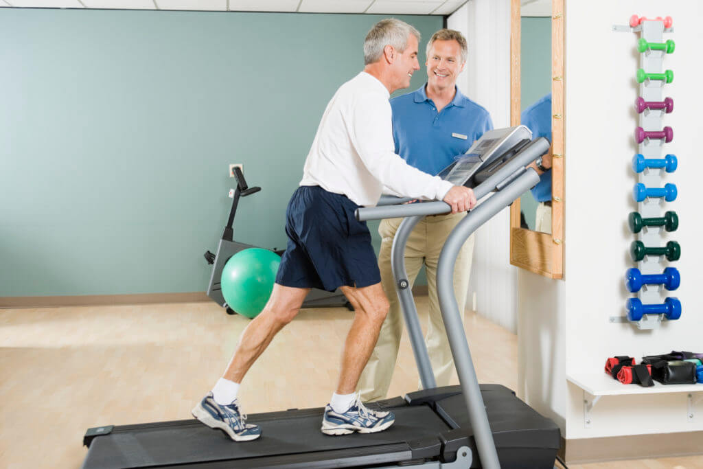 Physical trainer helping man on treadmill