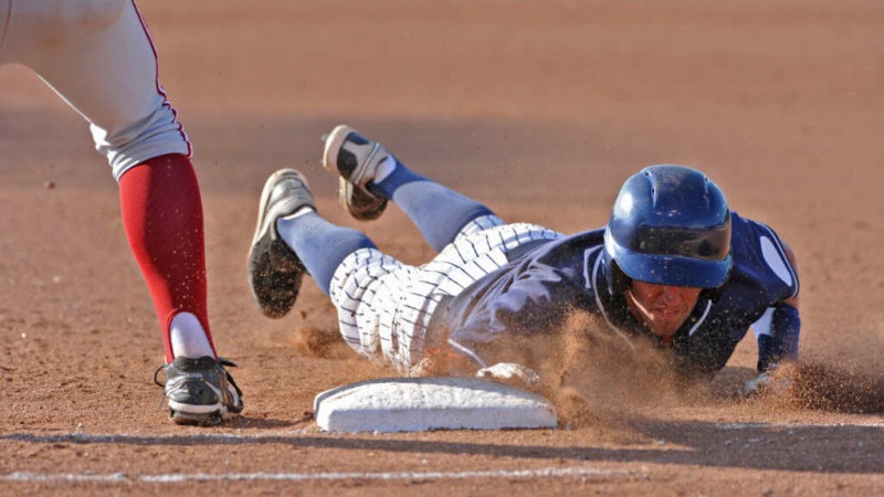 Man wearing a helmet slides into base during a baseball game. Concussion can happen even when athletes wear helmets.