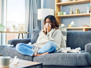 Shot of a young woman blowing her nose while sitting at home.