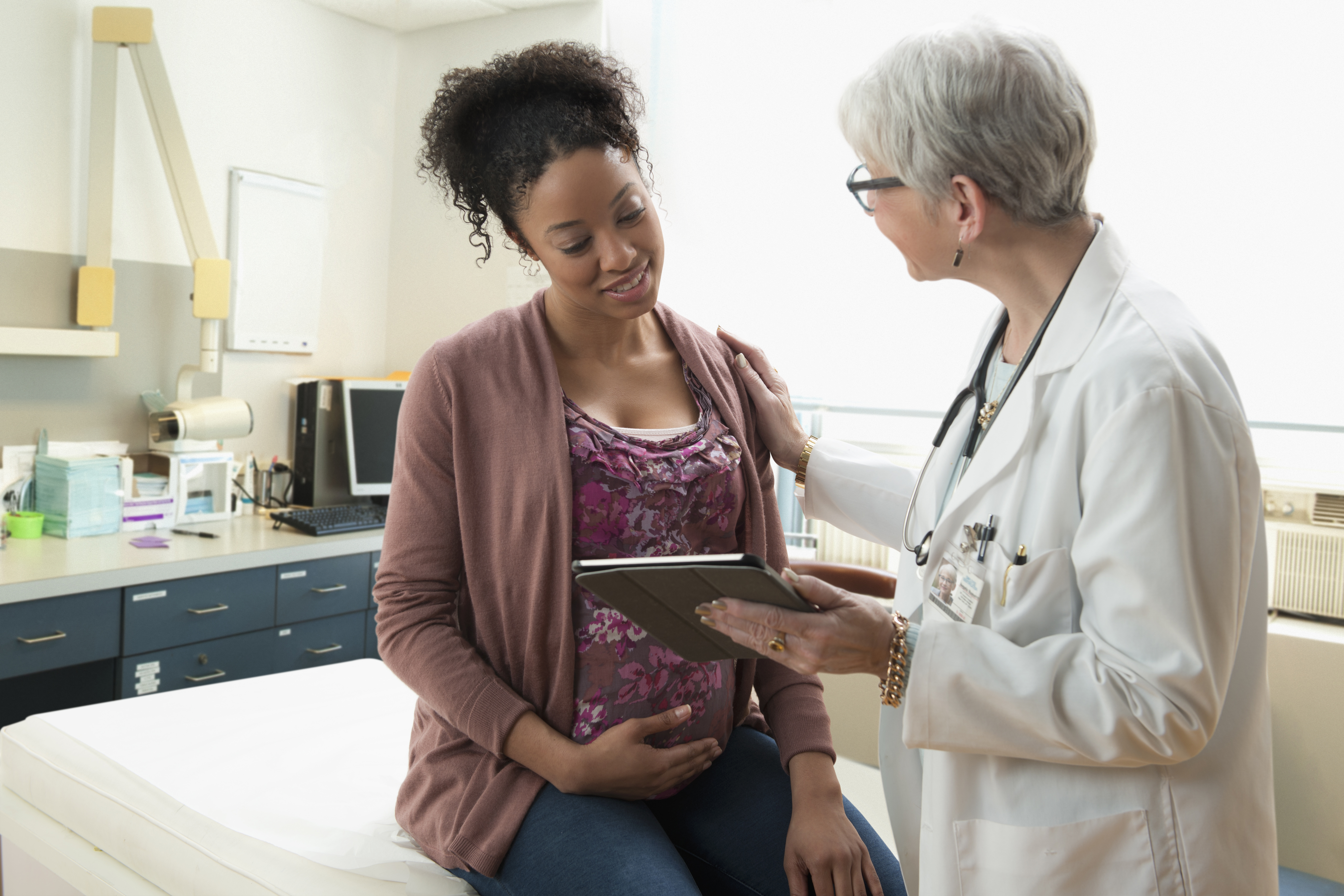 Gynecologist with digital tablet comforting pregnant patient