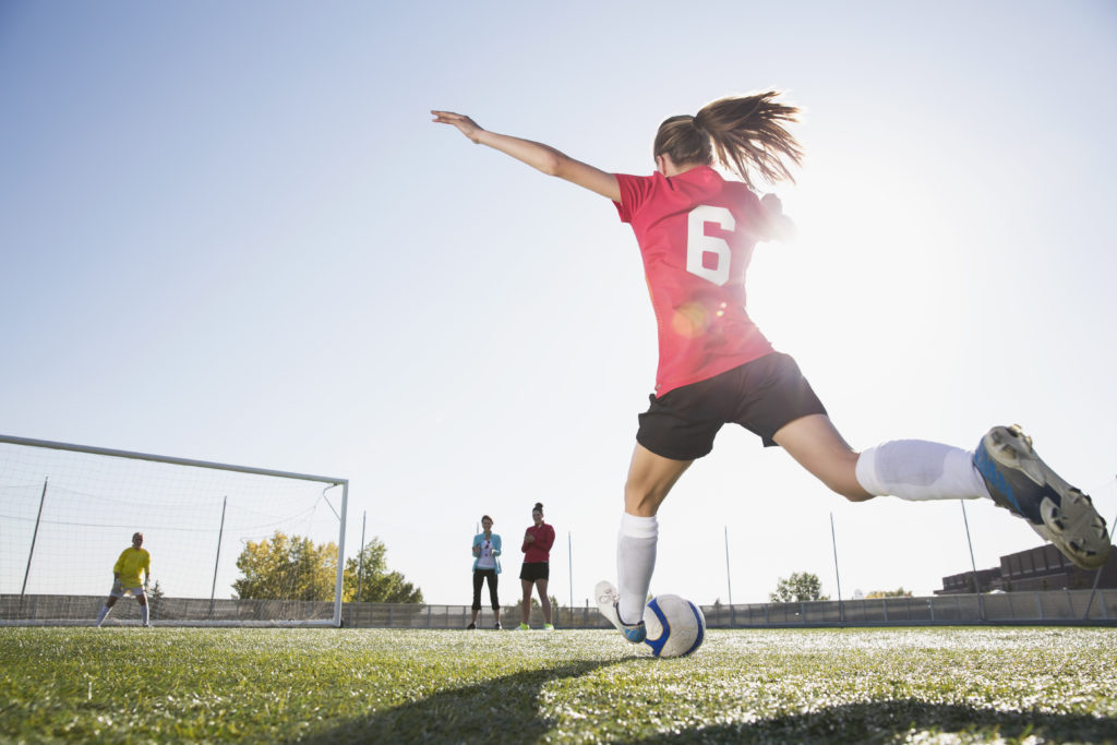 Female soccer player kicking soccer ball in goal