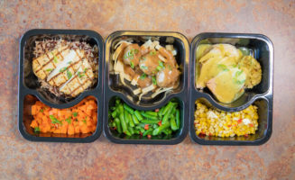Three plastic food storage containers with colorful meals and sides.