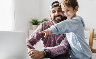 Dad and son signing up for insurance during open enrollment on his computer.