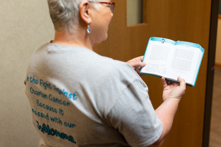 Joan Muller holds the daily devotional her Sanford Health co-workers wrote personal messages in while wearing the earrings Dr. Ashley Briggs made for her and the T-shirt, which was available for sale to co-workers, family and friends.