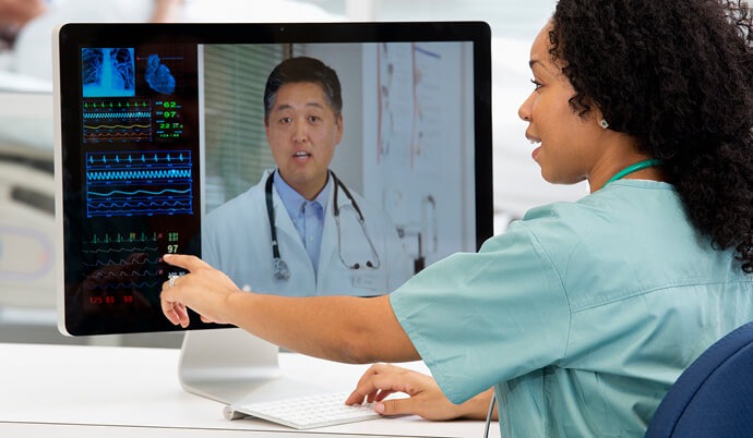 A telehealth nurse consults a doctor on a computer screen.