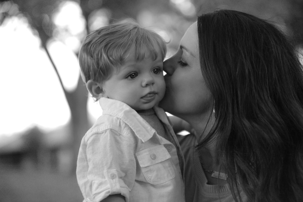 A mom kisses a toddler boy on the cheek. The mom's face is in profile.