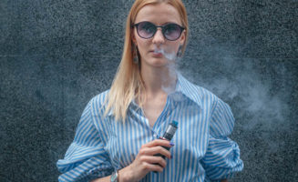 Teen girl with sunglasses uses an e-cigarette device.