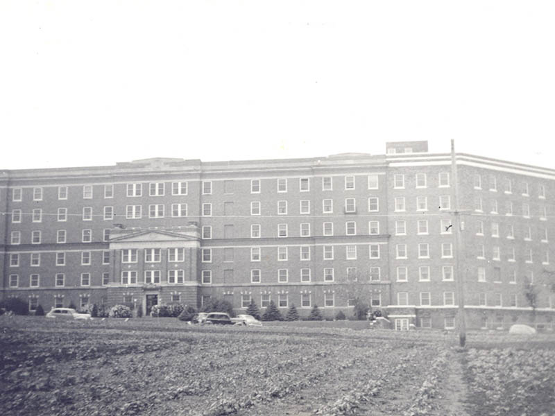 A planted field of crops stands in front of Sioux Valley Hospital in the mid-20th century.