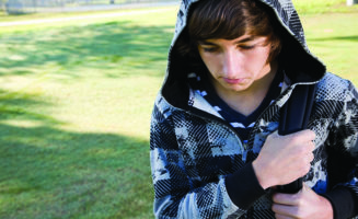 A teen school-age boy with a backpack looks downtrodden.