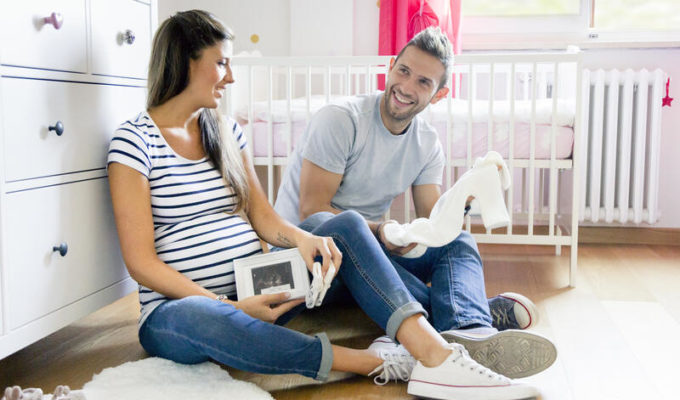 Pregnant couple sitting on floor in nursery preparing baby clothes.