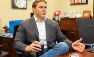Bill Gassen in mid conversation, sits in his office and holds a water bottle.