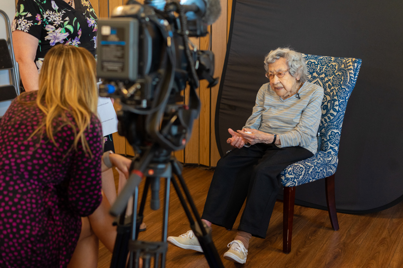 A television news reporter interviews Julia Kabance at her 109th birthday party.