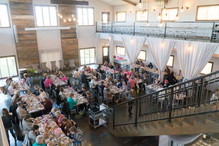 Women sit at long tables in an events center as they dine and attend a retreat for breast cancer survivors.