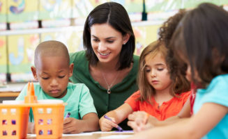 ABA classroom setting. Group of elementary age children in art class with teacher sitting down at table, drawing.