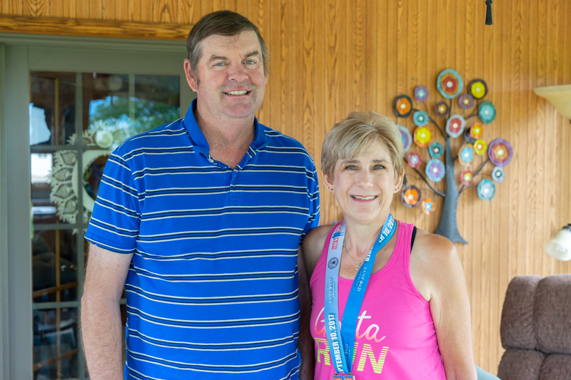 Randy and Deb Warner stand in their wood-paneled four-season room. Deb wears her Sioux Falls half-marathon medal.