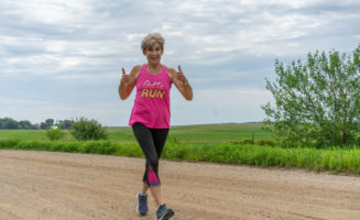 Deb Warner gives two thumbs-up signs as she runs on a gravel road. Her shirt says "gotta run."