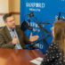 Pat Kelly speaking into a microphone in front of Jacqueline Palfy