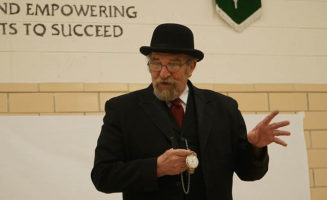 Steve Stark, aka Mr. History, stands in front of a classroom wearing a black frock coat, black hat and holding a pocketwatch.