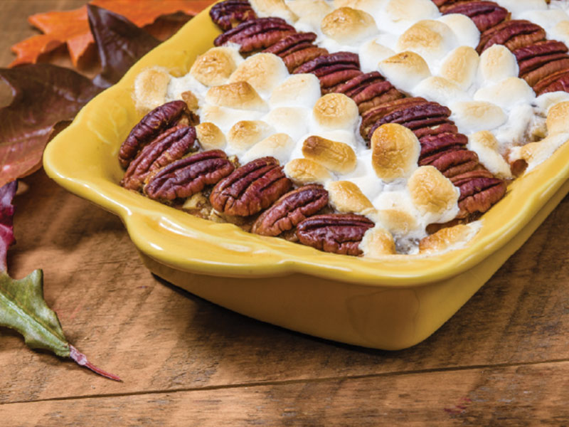 Butternut squash casserole topped with pecans and marshmallows in a yellow dish.