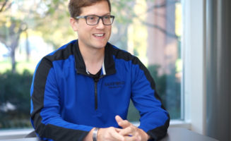 Jeff Pratt smiles and sits at a conference table with a garden view behind him.