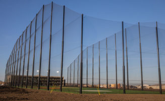 Fencing towers over the Great Shots golf complex, seen under a blue sky.