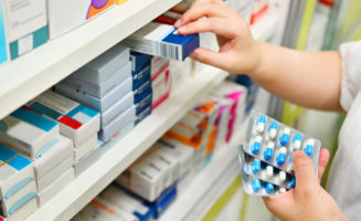 Pharmacist holding medicine box and capsule pack in pharmacy drugstore.