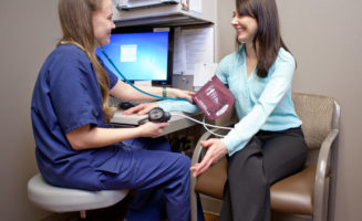 A nurse takes the blood pressure of a smiling adult woman patient.