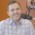 Nate Malloy smiles as he speaks into a microphone in an orange office.