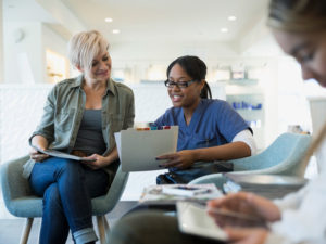 A menopausal woman sits in a waiting room looking over her medical records with a nurse.