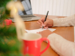 man wearing cream sweater writing christmas letter greeting card holiday wishes with xmas decoration.