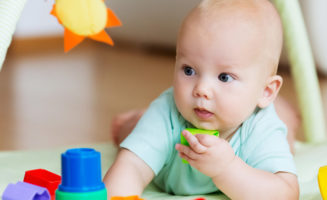 6-12-month-old baby plays with blocks while lying on the floor.