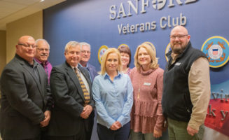 veterans affairs: Group of men and women smile while standing in front of sign for Sanford Veterans Club.