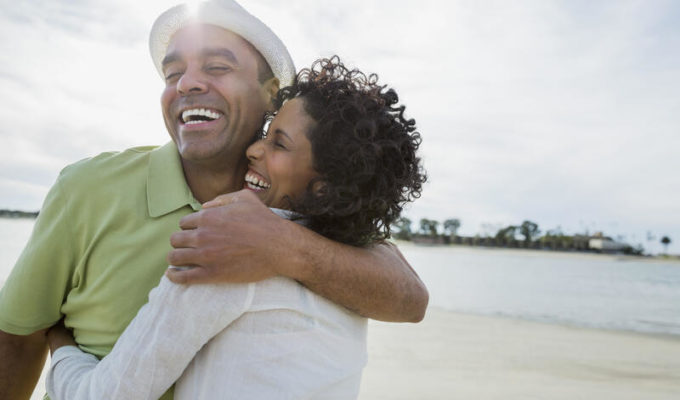 A happy, healthy mid-40s couple hugs on a sunny beach.