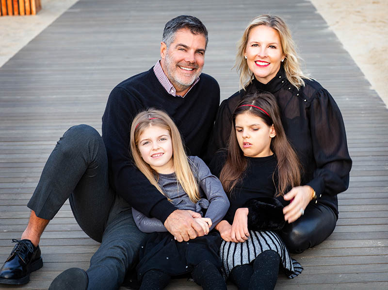 Gordon and Kristen Gray sit on a boardwalk with their daughters Gwenyth and Charlotte on their laps.