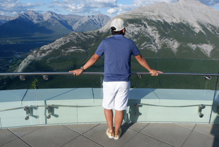 Jerico Alicante stands looking at rocky Mountains with back to camera.