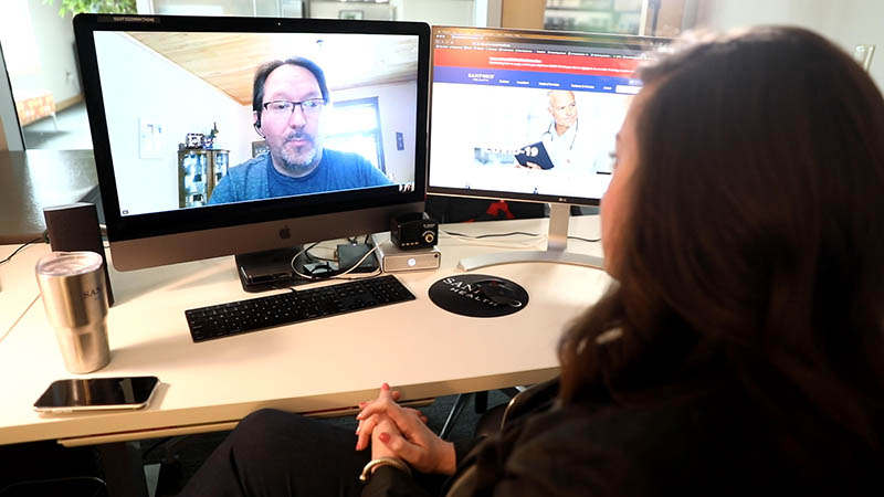 Bob Goettle, seen on a computer screen, talks via video chat with Sanford Health News multimedia journalist Courtney Collen, whose back is to the camera. 