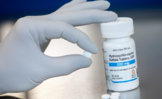A gloved hand holds a hydroxychloroquine pill, which will be used in a clinical trial