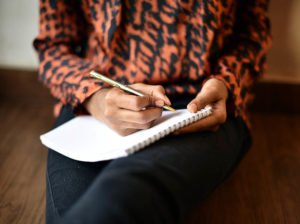A woman holds a pen and notepad on her lap, in a portrait of journaling
