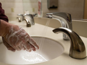 A man's hands are covered in soap in front of a faucet to illustrate hand hygiene.