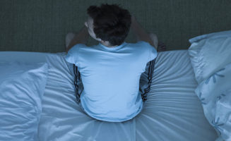 A man sits up on the edge of his bed, after not getting good sleep