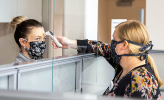 A female Sanford Health worker reaches over a partition to take the temperature of a woman in a face mask.
