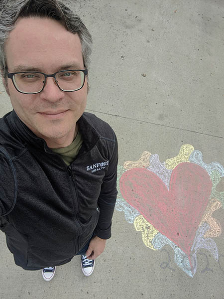 Andrew Larson stands for a self-portrait that includes a sidewalk chalk drawing of a heart with "2020"