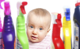 A baby peers out from the middle of bottles of cleaning supplies